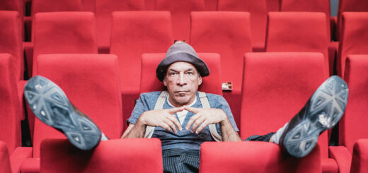 Peter Shub con sombrero, sentado entre las butacas rojas de un teatro.