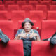 Peter Shub con sombrero, sentado entre las butacas rojas de un teatro.